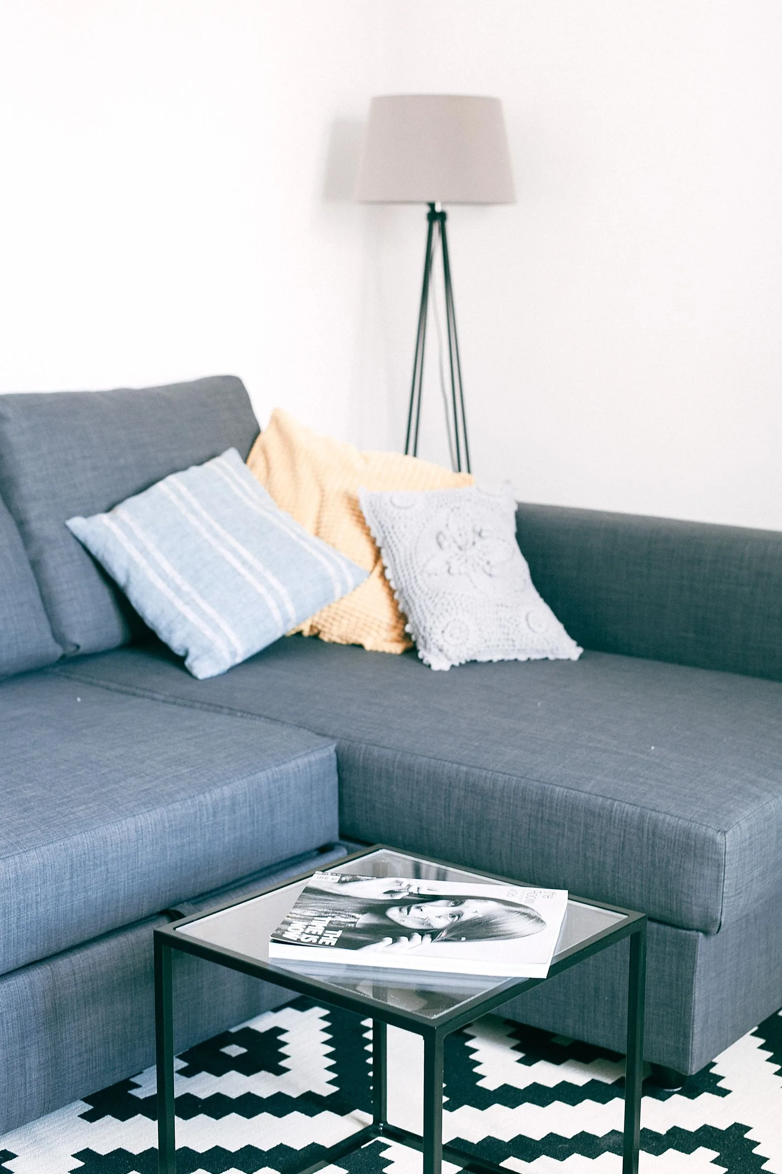 Salon moderne avec canapé gris anthracite et coussins textiles variés sur tapis géométrique noir et blanc, exemple d'intégration des textiles dans un appartement contemporain