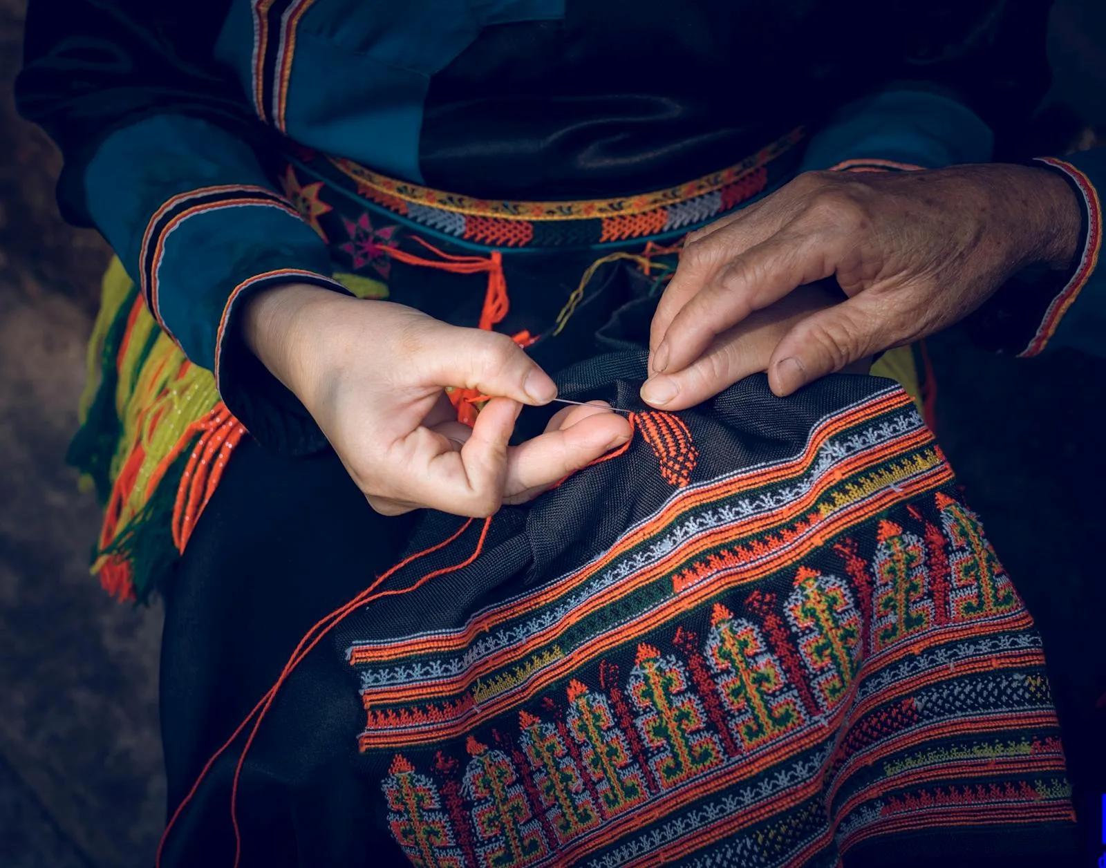 Mains d'une artisane brodant un vêtement traditionnel avec des fils de couleurs vives — broderie ethnique réalisée à la main