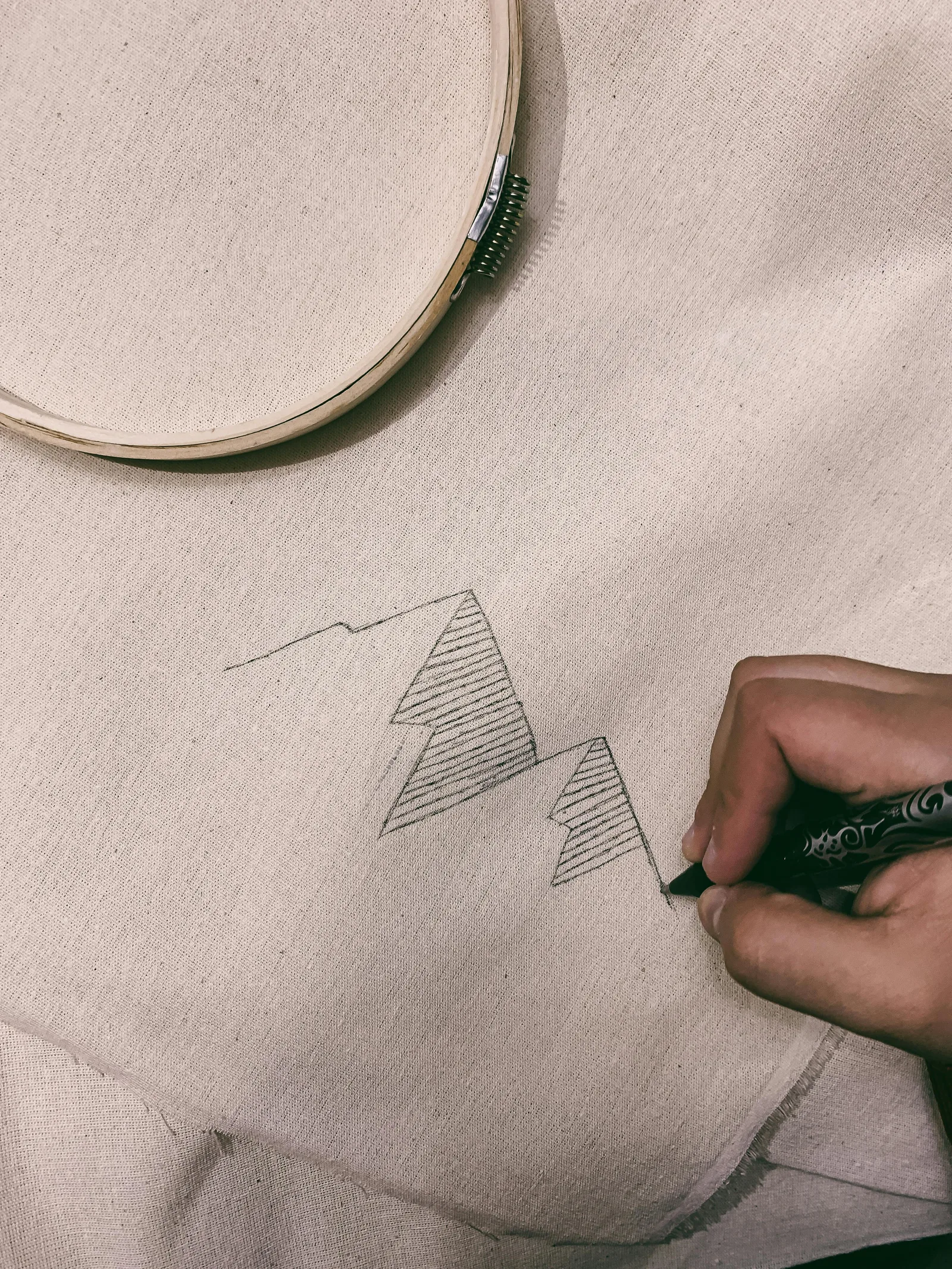 main dessinant un motif géométrique de montagnes sur tissu lin pour broderie minimaliste avec cerceau en arrière-plan