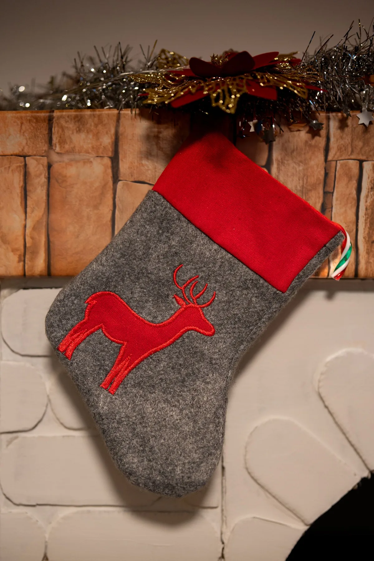 Chaussette de Noël brodée d'un renne rouge suspendue devant une cheminée décorée