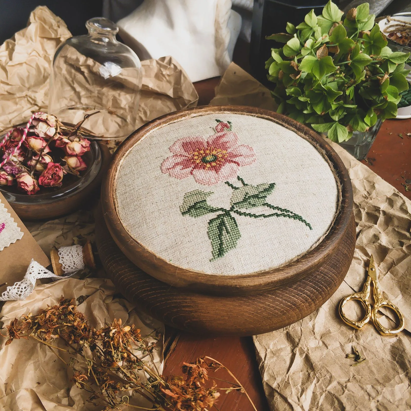 Cerceau de broderie en bois avec motif floral délicat sur lin, entouré d'accessoires de broderie et fleurs séchées dorées