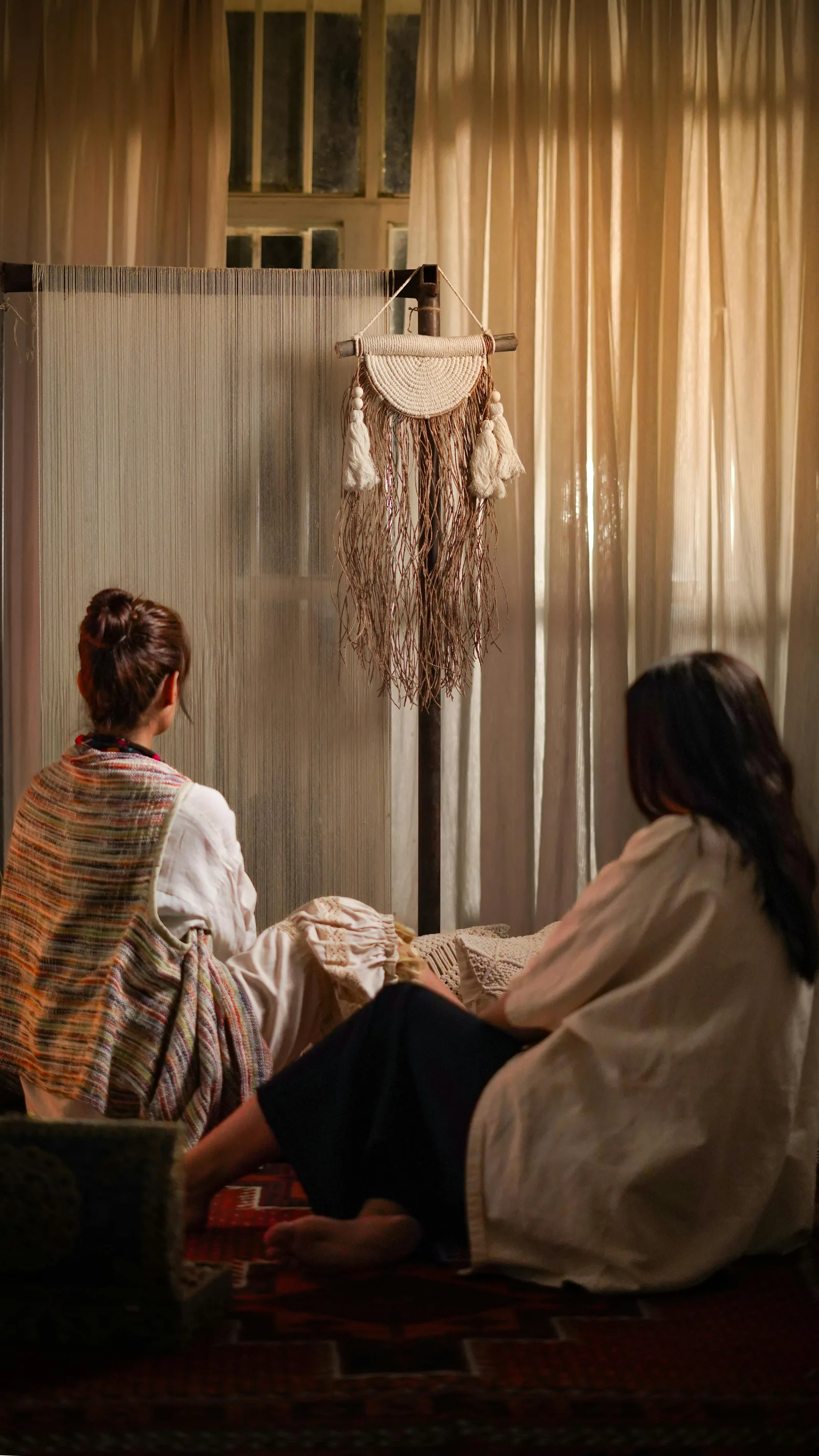Deux jeunes femmes dans une ambiance cosy avec textiles et art textile bohème au mur