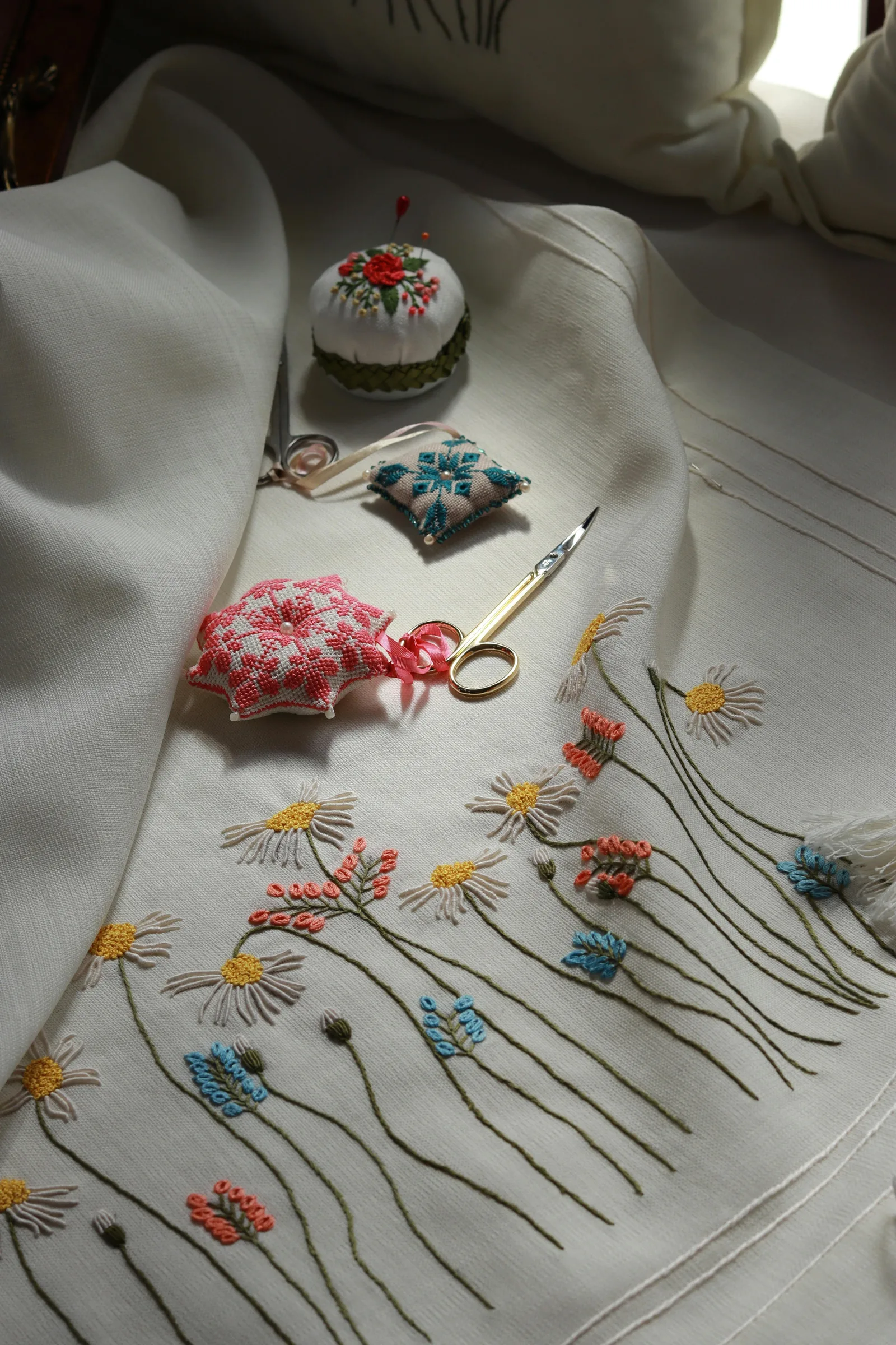Pelotes brodées, ciseaux et linge brodé de marguerites — les accessoires de la brodeuse au service de la déco chambre