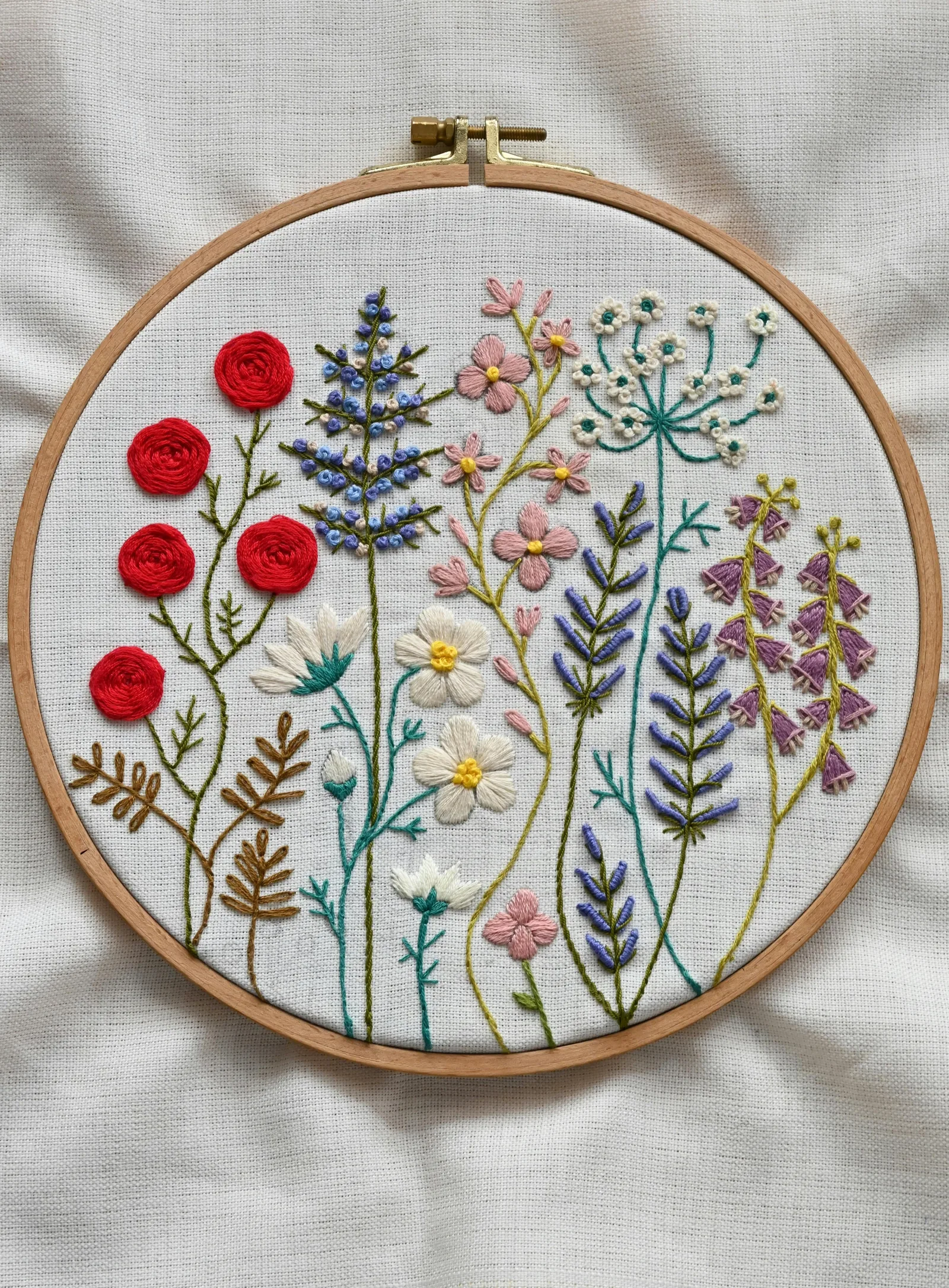 Cerceau de broderie avec composition florale botanique colorée — roses rouges, marguerites blanches, lavande et feuillage