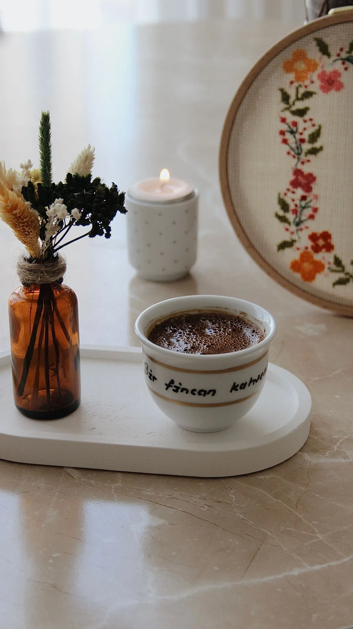 Cerceau brodé de fleurs suspendu au-dessus d'un plateau avec tasse de café fumante sur une table en marbre