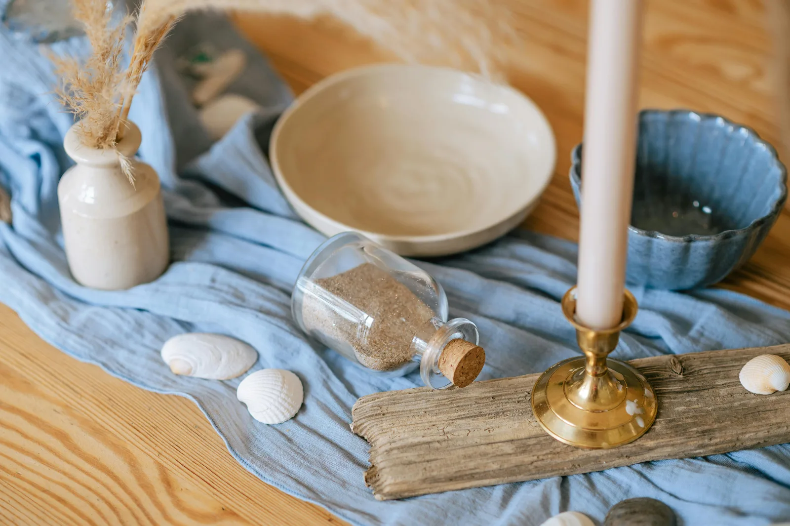 Table en bois avec textiles bleus, bougie sur bois flotté, coquillages et bouteille de sable, ambiance déco bord de mer