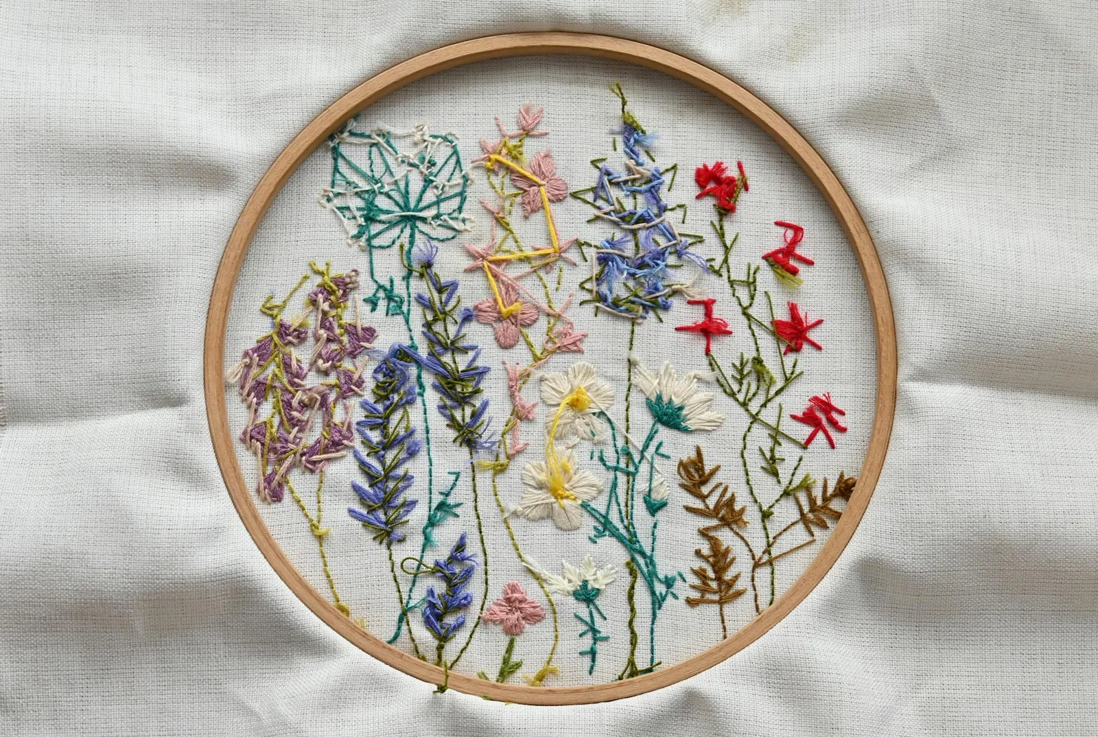 Broderie de fleurs sauvages champêtres en point de croix dans un cerceau en bois sur fond de tissu