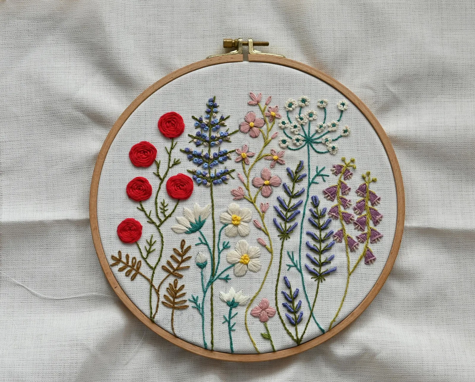 Broderie florale dans un cerceau en bois avec marguerites et fleurs champêtres en point de croix