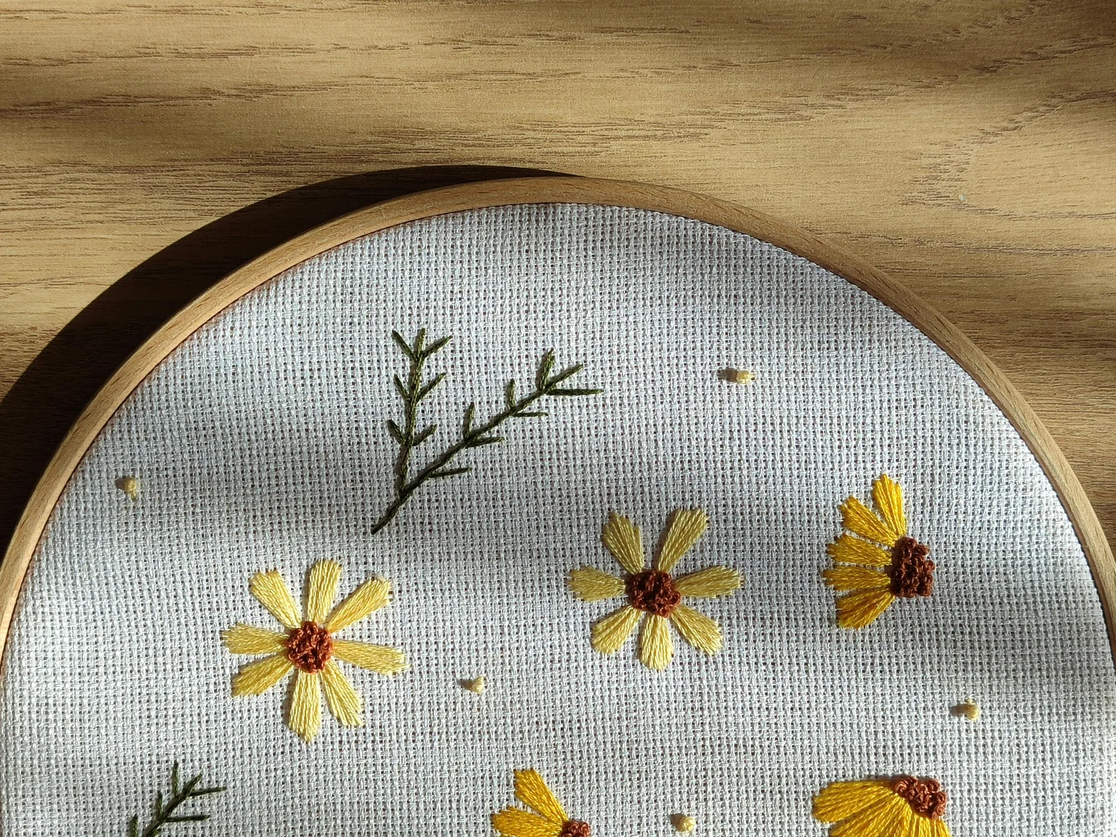 Cerceau de broderie avec motif floral jaune sur toile bleue pâle, exemple de finition hoop art