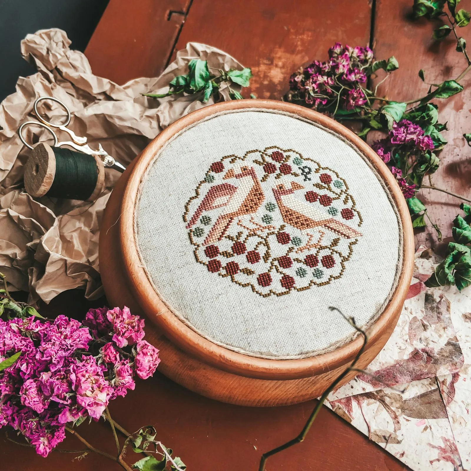 Cerceau de broderie point de croix avec deux oiseaux stylisés — composition florale en tons terracotta et bordeaux
