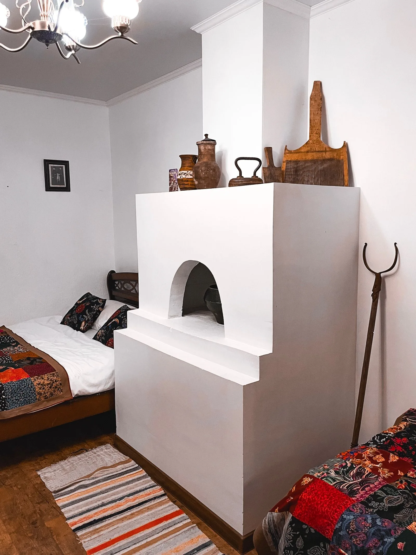 Chambre rustique avec textiles brodés colorés sur lit en bois, poêle blanc traditionnel et parquet ancien