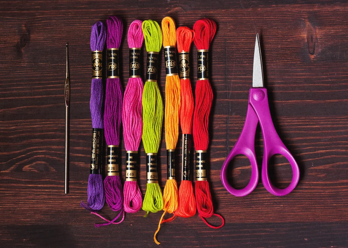 Fils de broderie DMC colorés, aiguille et ciseaux pour broder un monogramme en point de croix