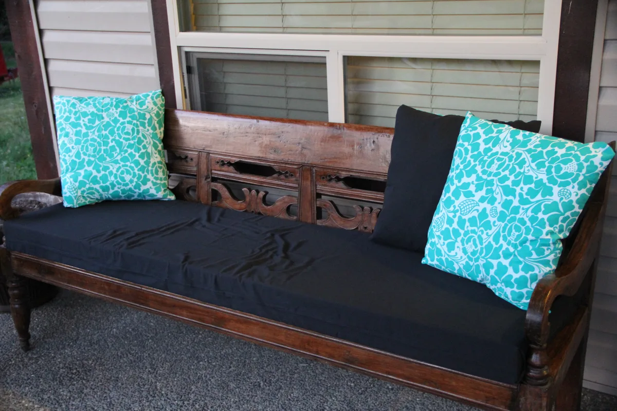 banc en bois sculpté de style asiatique sur terrasse extérieure avec coussins brodés turquoise aux motifs floraux