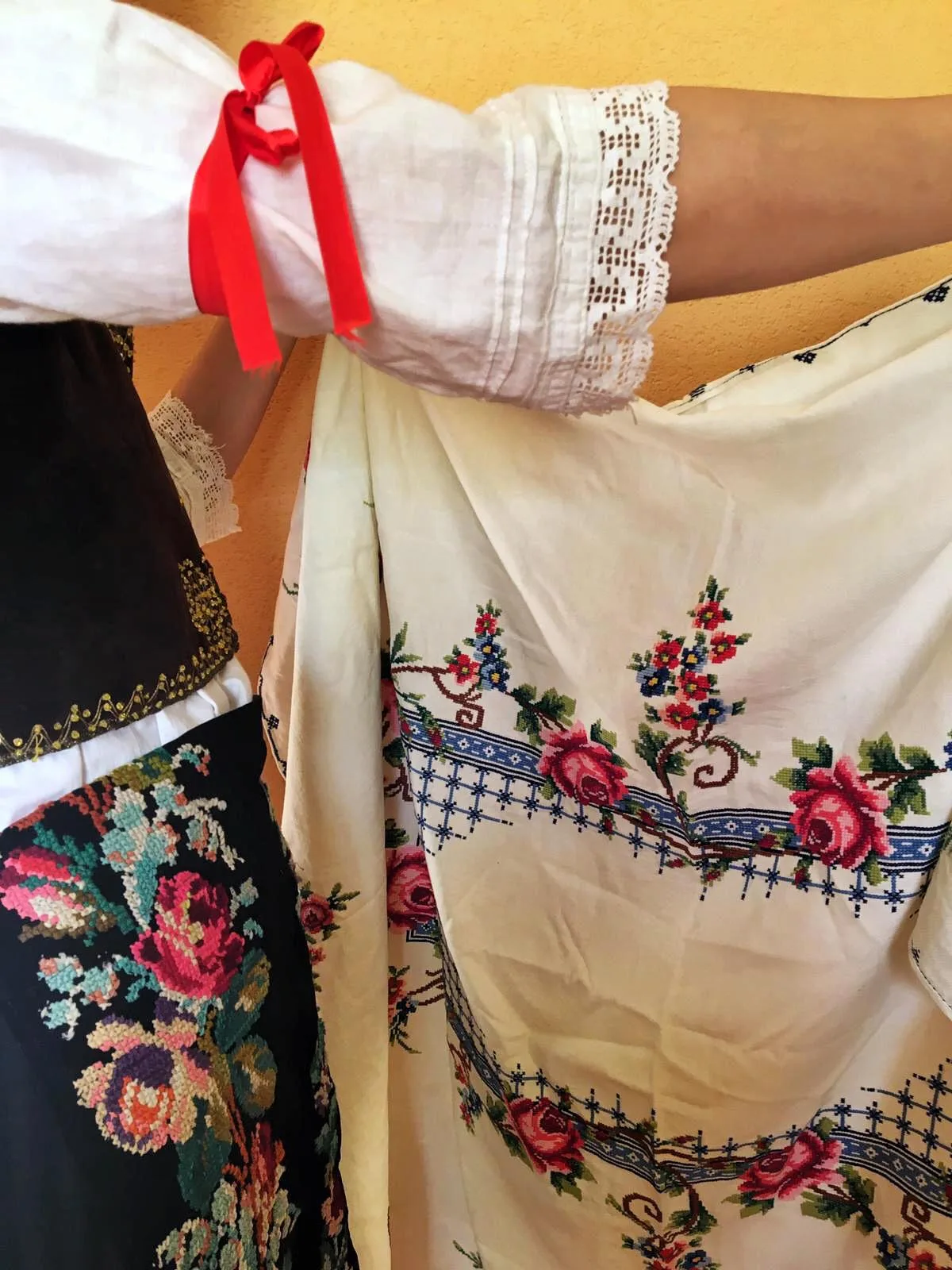 Broderie traditionnelle en point de croix sur textile blanc avec motifs de roses rouges et bleues, style folk européen