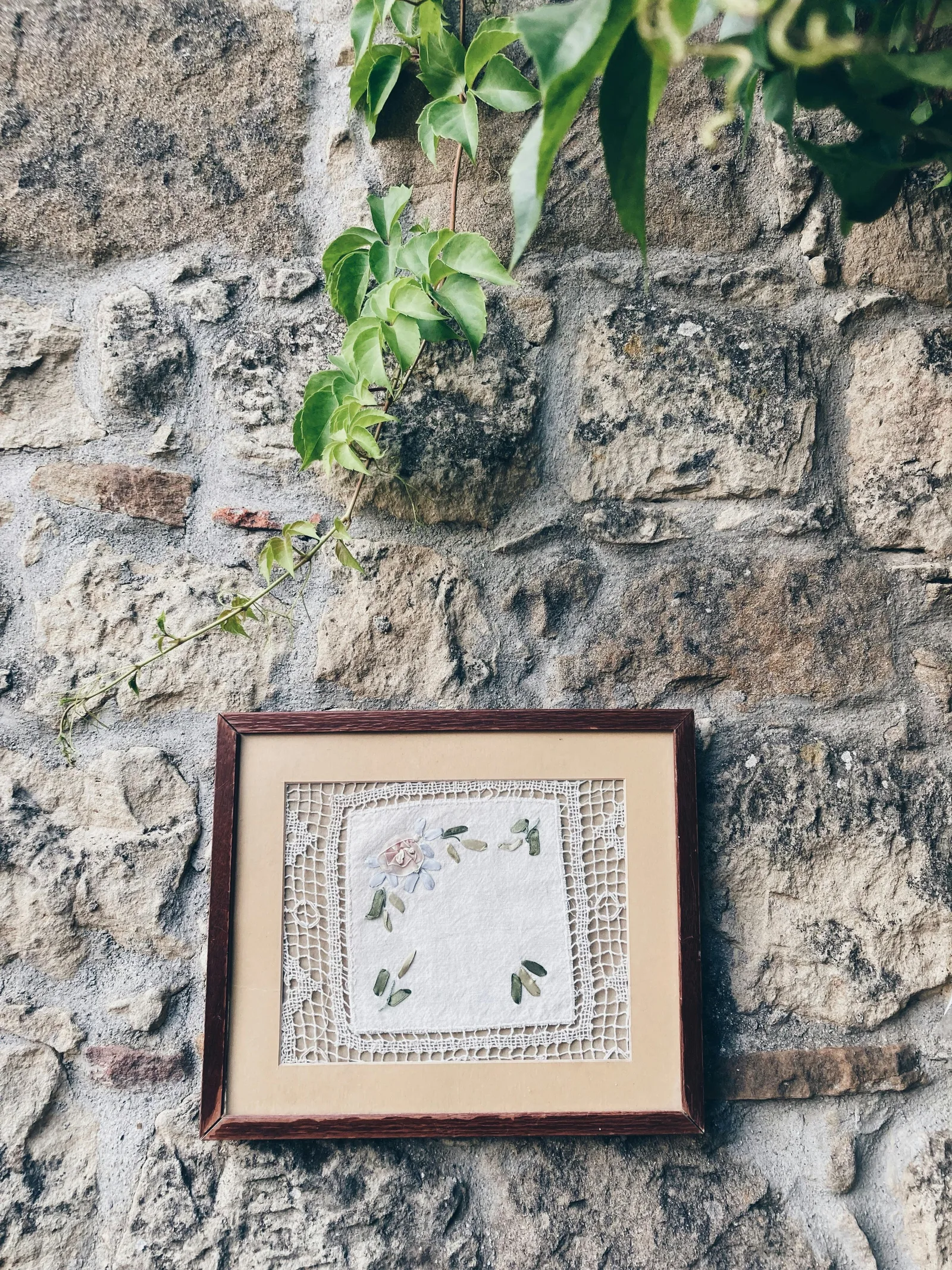 Cadre brodé floral accroché sur mur en pierre rustique — décoration murale avec broderie encadrée dans un intérieur naturel
