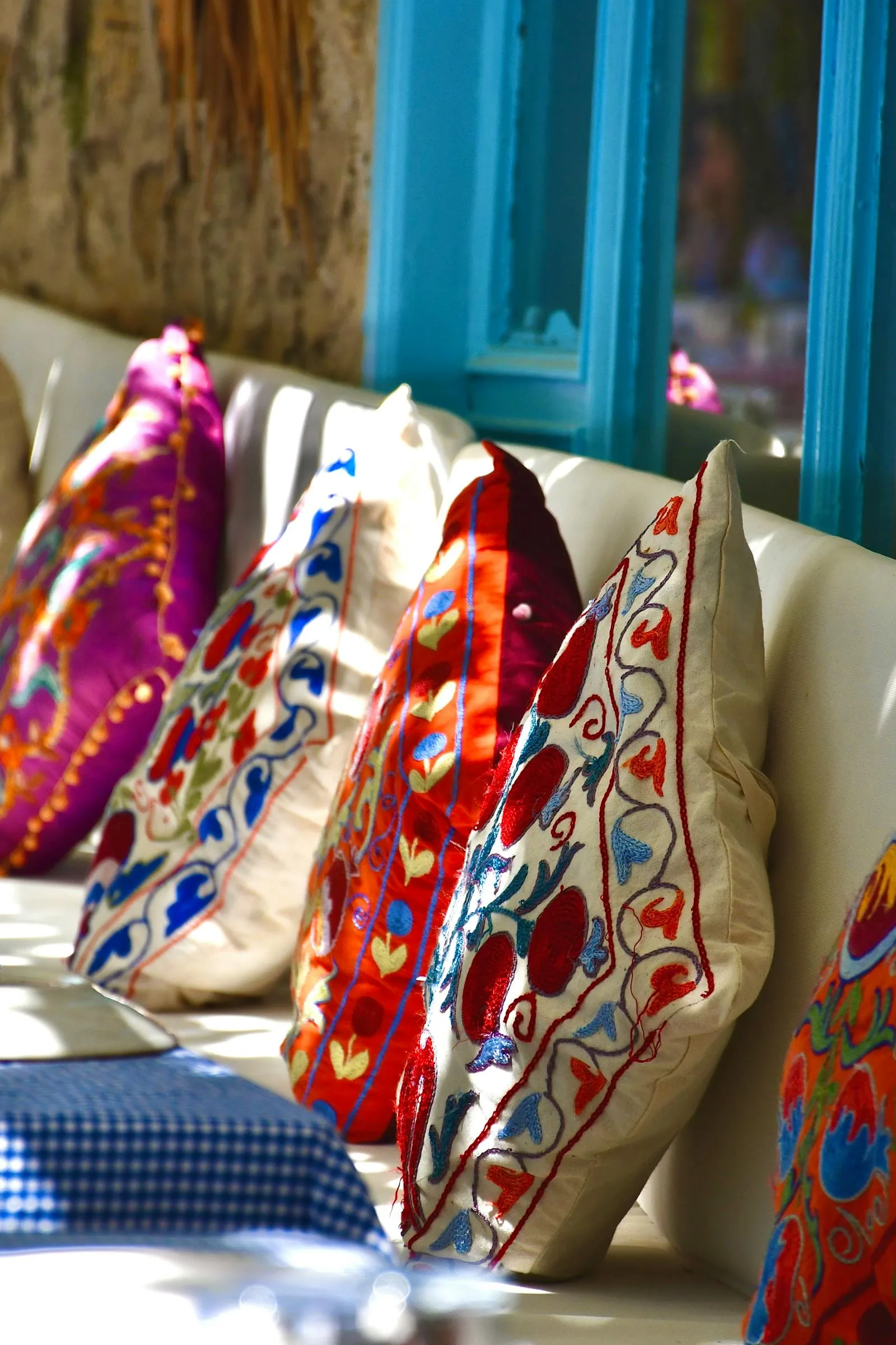 coussins brodés suzani aux motifs floraux colorés disposés sur un banc de terrasse méditerranéenne
